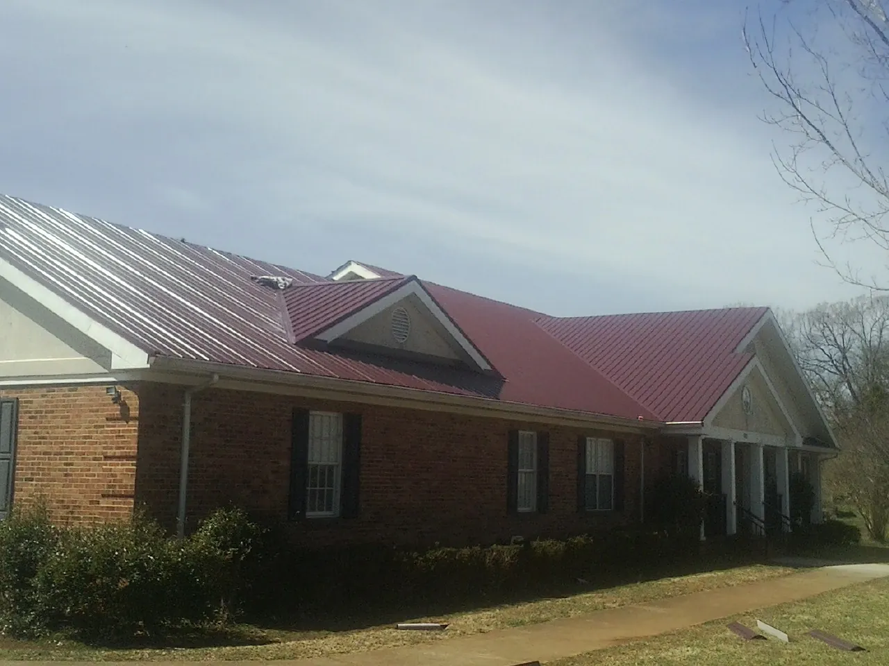 Red metal roof with gabled entries on a long brick building, from a Hail Damage Roof Repair job in Coraopolis