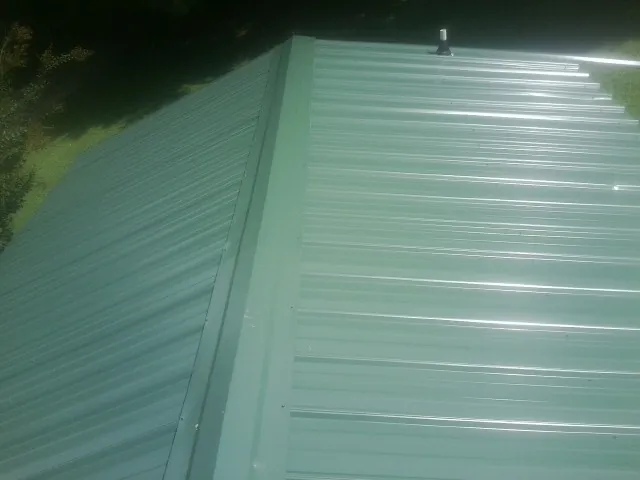 New green metal panels meeting at the ridge of a roof — Flat Roof Repair work by our crew in Coraopolis