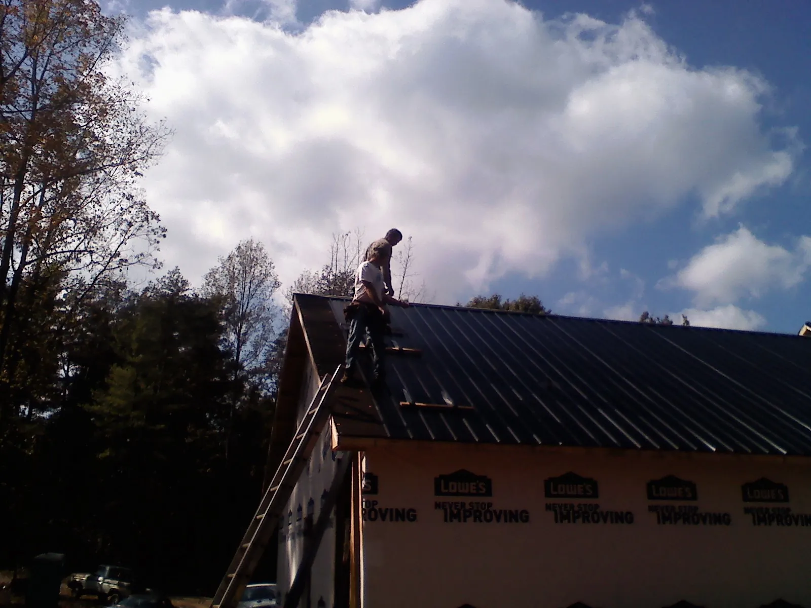 Roofer fastening dark metal panels high against a cloudy sky, from a Roof Inspection job in Coraopolis