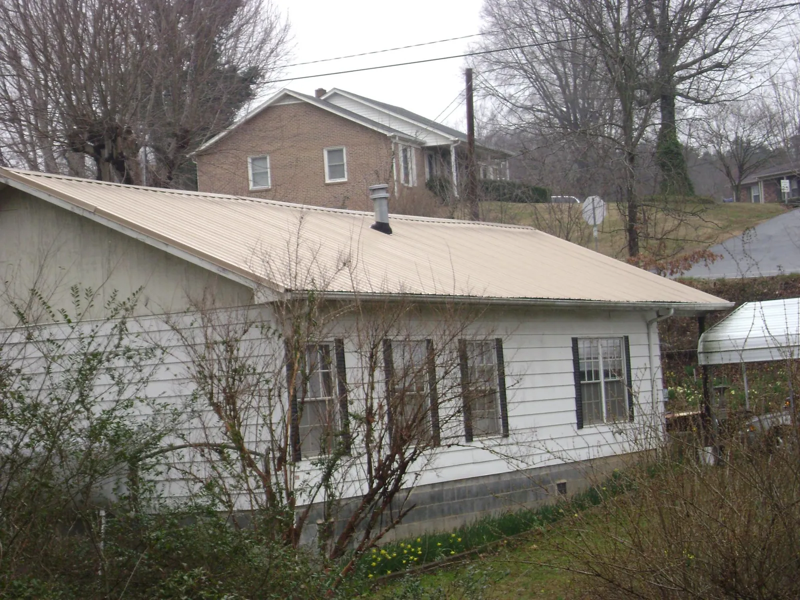 Tan metal roof on a white sided house set into a hillside — Commercial Roofing by Roofing Brothers in Coraopolis